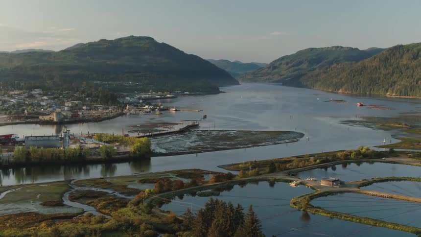 A serene coastal landscape with a winding river flowing through a lush green valley towards a town nestled between rolling hills