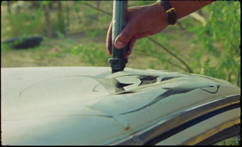 A persons hand using a black marker to draw on the surface of a car body