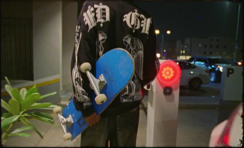 Four teenagers with skateboards walking on a sidewalk next to parked cars