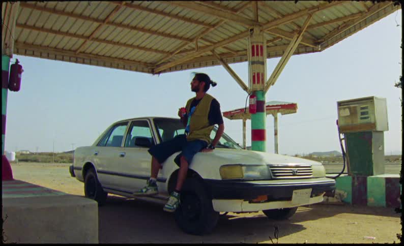 Man sitting on a car hood at a gas station