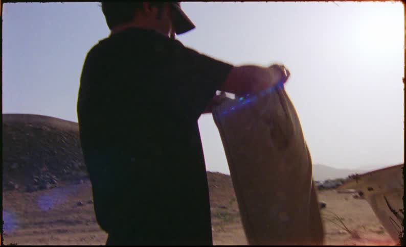 Man examines clothes taken from a trunk while standing in the desert on a sunny day