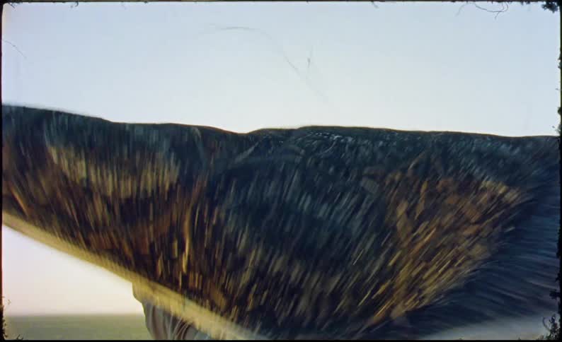 A man with tied hair is holding a large piece of cloth above his head and the cloth is moving quickly because of the wind