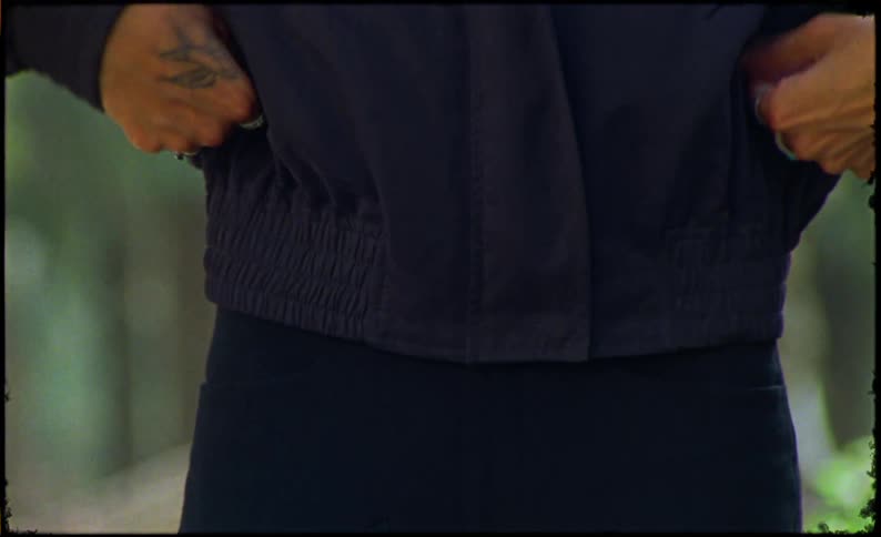 A young man with a butterfly tattoo and wearing multiple rings in his hands zips up a dark jacket