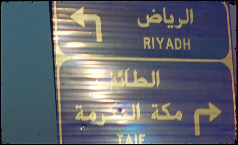 A blue road sign with white text and arrows indicating directions in arabic
