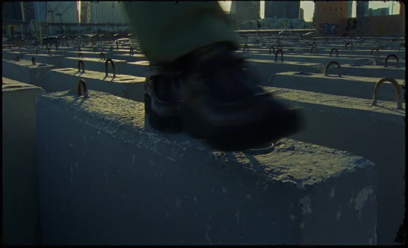 The legs of a person in green pants and black sneakers walking on concrete blocks