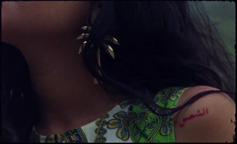 Womans hair blows in the breeze showing off her shoulder tattoo and palm tree earring