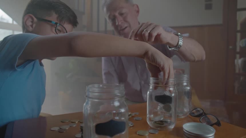 A boy and an elderly man sort coins into glass jars at a table