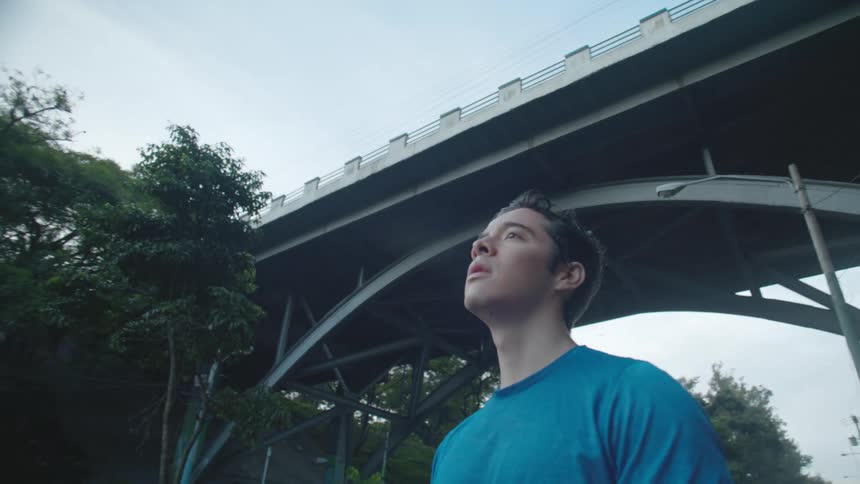 Man standing near an bridge straightens his arm while a car passes