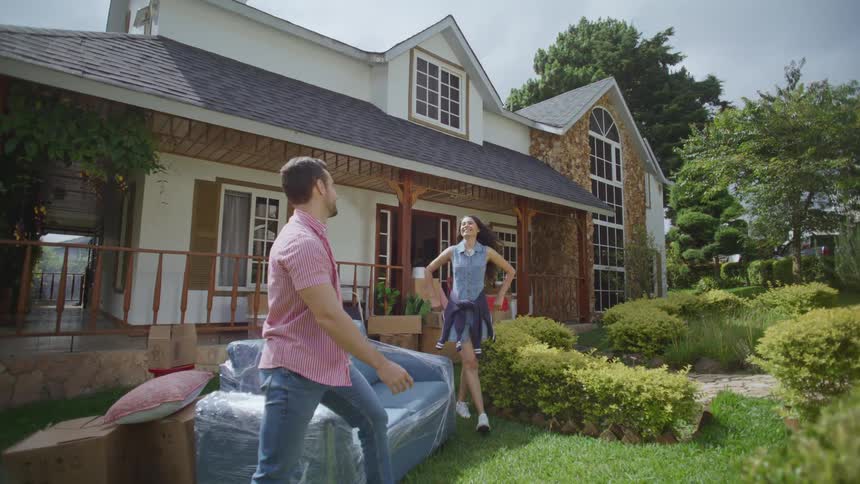 Happy couple taking a break on couch in front of new house while moving