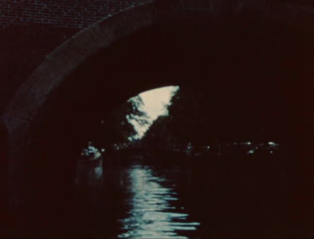 A dark scene under a bridge showcasing a canal illuminated by faint light