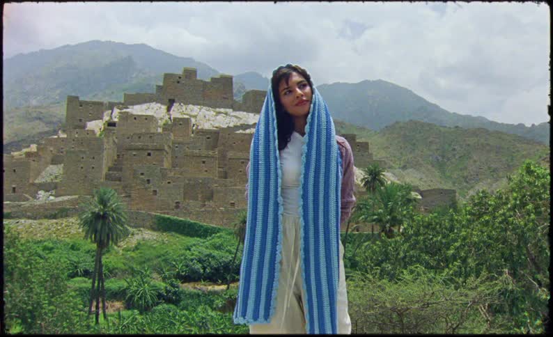 Woman wearing a head cover smiles while turning to look at a historic building