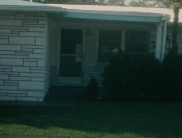 A vintage sedan sits in a driveway partially obscured by a pillar