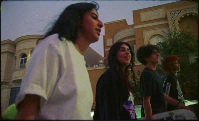 A group of 4 teenagers with skate boards run down a city road at sunset