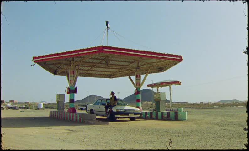 A man is sitting on his car at the gas station