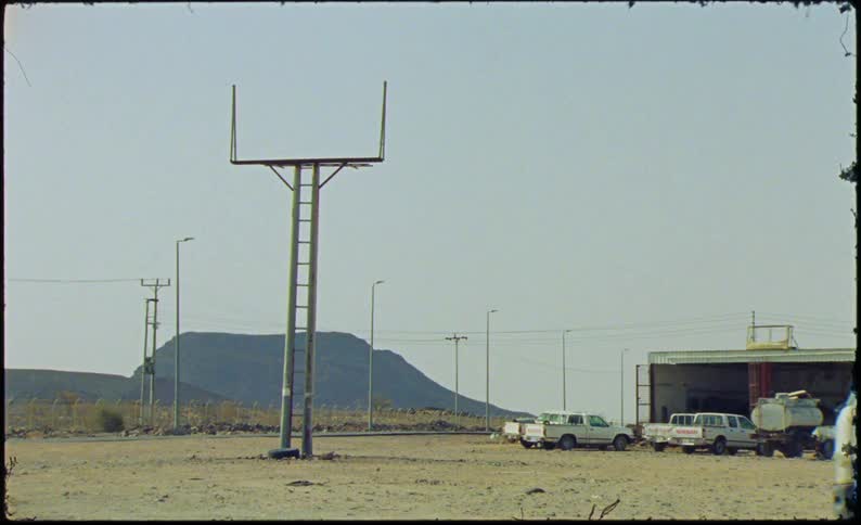 Parked cars in the background of a truck passing by a road with mountains in the background