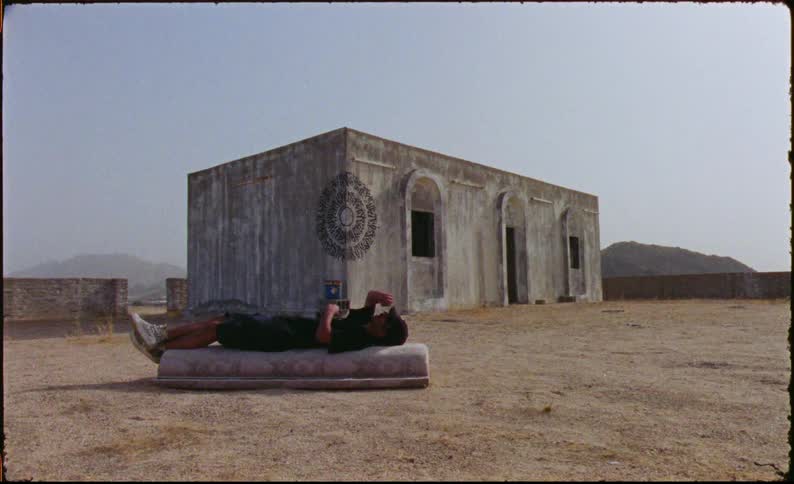 Man lying on a mattress in an outdoor area next to an ancient structure
