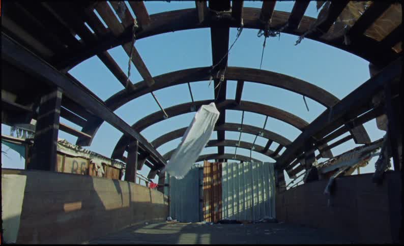 A dilapidated wooden boat with a hanging white garment and a clear blue sky visible through the damaged roof