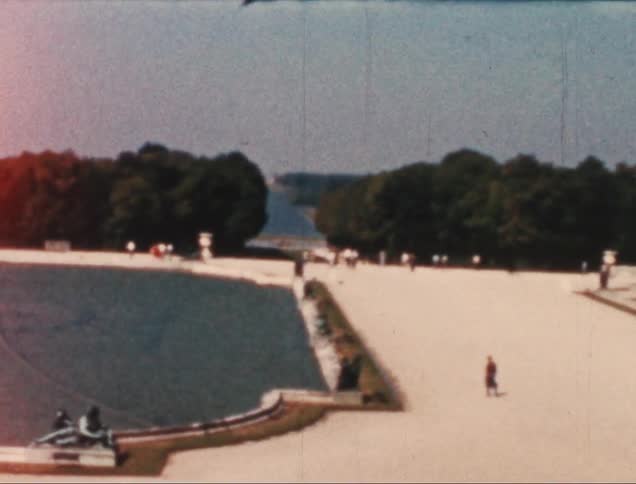 People walking through a park with a fountain and trees in the background