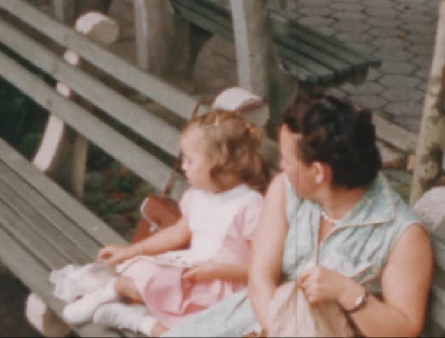 A child and her mother are sitting on a park bench having lunch