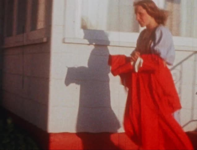 A woman in a dress carrying a red jacket walks down stairs outside of a house