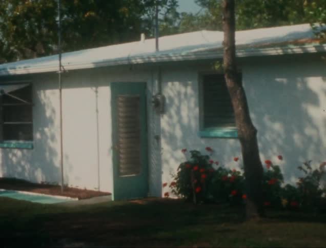 A small singlestory house with a white exterior a turquoise door and a striped awning over a window
