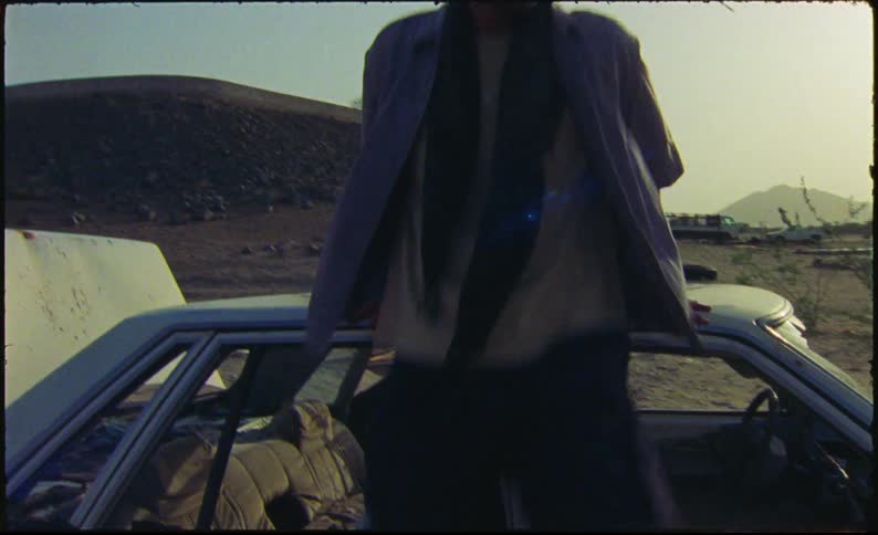 Man walking and sitting on the roof of a car in a desert location
