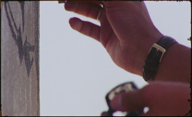 A male with a watch uses a paint pen on a wall for graffiti