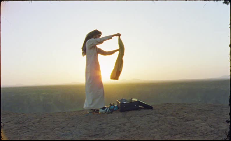 Man pulls pants from a suitcase and refolds them while in the desert at sunrise