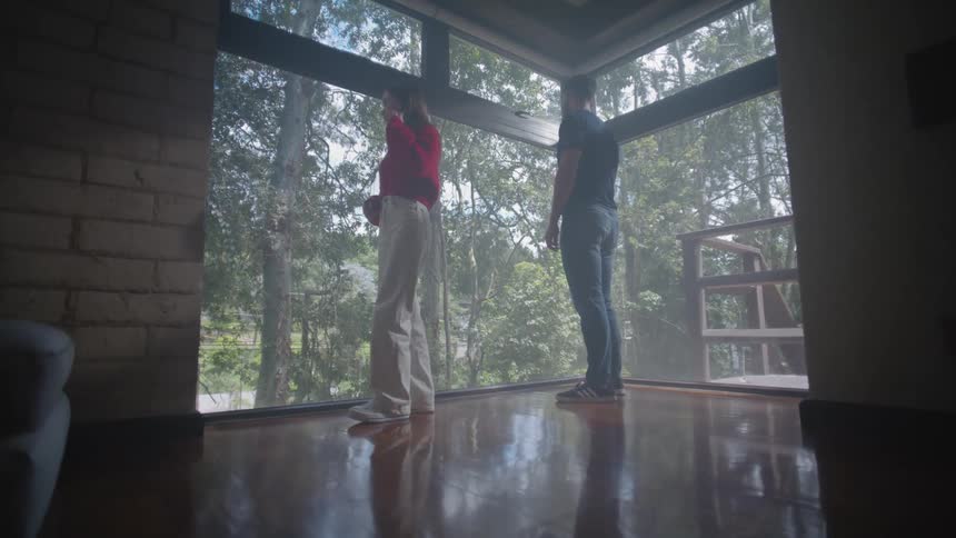 Man and woman in an indoor space next to a large window with trees in the background