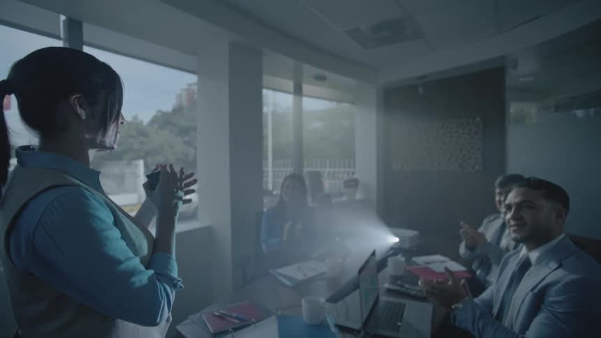 A woman in front of a projector with a group clapping