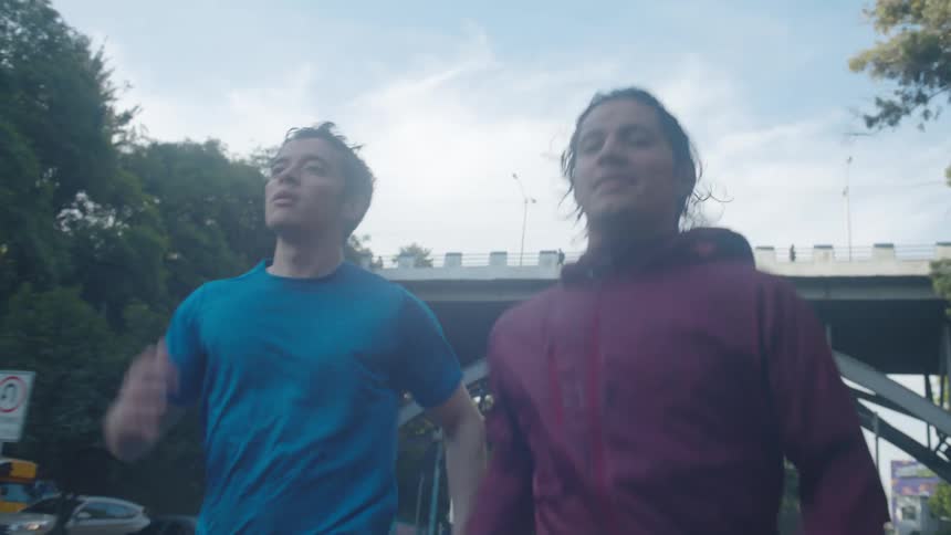 Two people are jogging on a road with trees and an overpass in the background