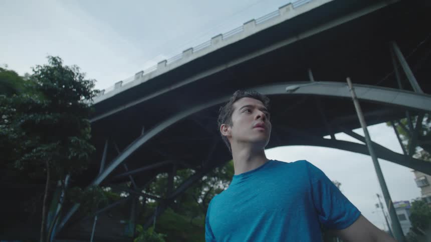 A man wearing a blue shirt is exercising beneath a bridge emphasizing fitness in a city setting