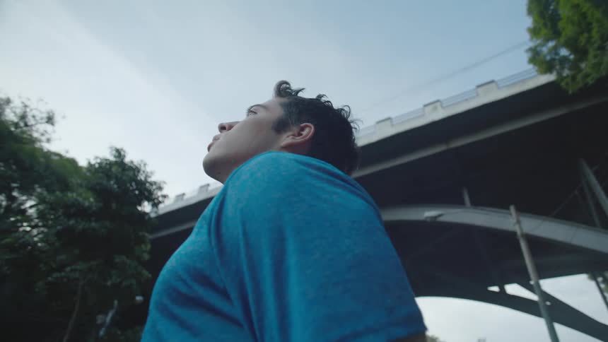 Male teenager stands near the base of an arched bridge looking up toward the sky