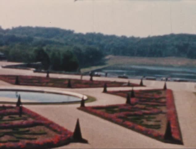 A large courtyard decorated with trees and concrete paths leading to a small body of water in the center