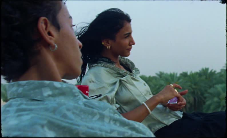 Couple having a conversation while relaxing on a roof overlooking the jungle while a woman gets ready to apply makeup