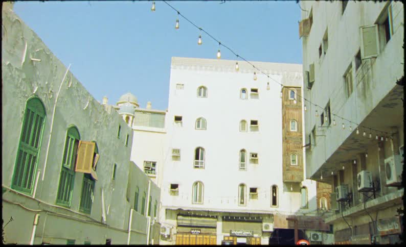 A narrow street lined with traditional whitewashed buildings with intricate wooden balconies and small windows