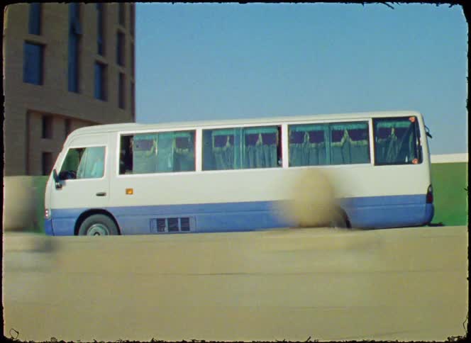 Small bus with curtained windows drives past an office building during the daytime
