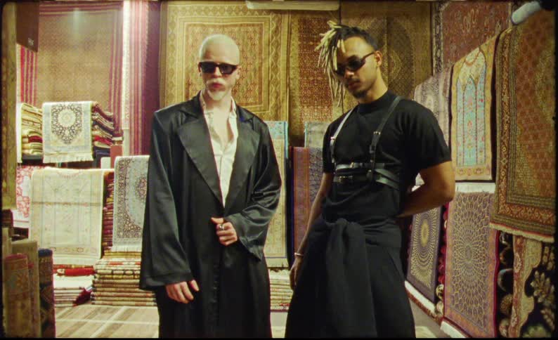 Two men in black outfits and blazers posing in a carpet store