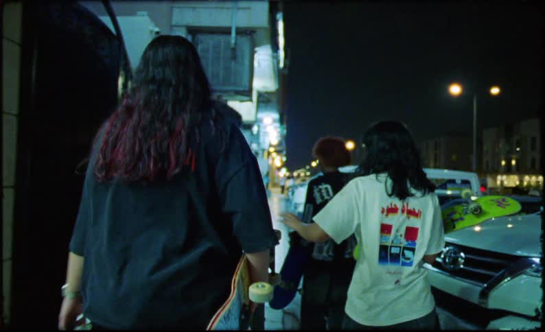 Group of teenagers walking with a skateboard in their hands next to cars through the city at night