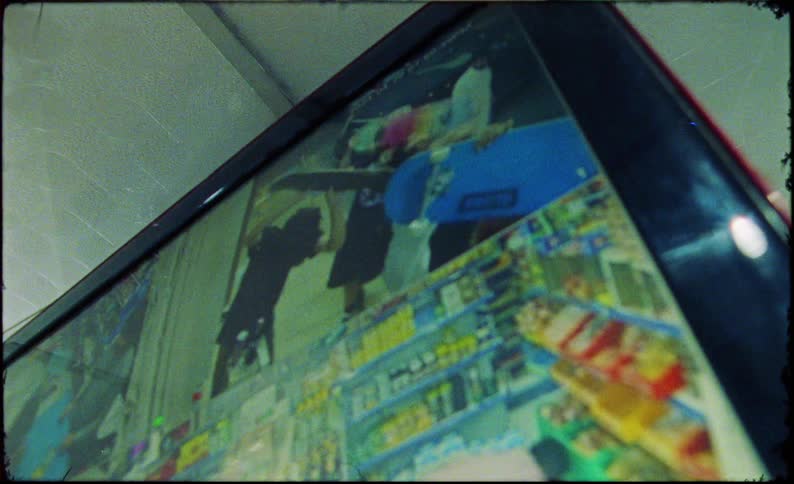 A security camera feed displaying a group of teenagers holding skateboards and posing in a store aisle