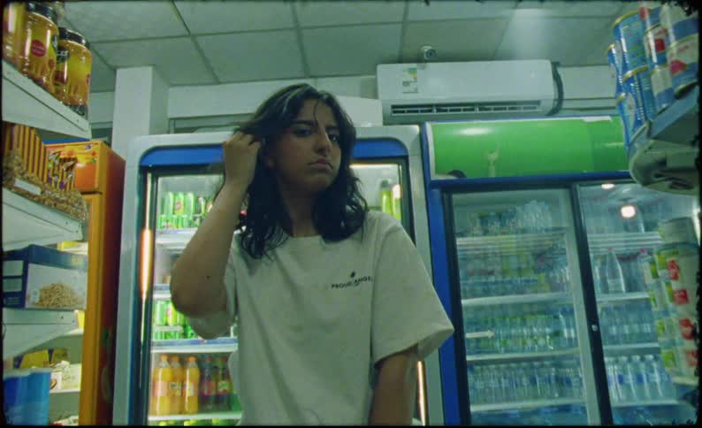 A teenage girl stands in a grocery store while holding a green skateboard