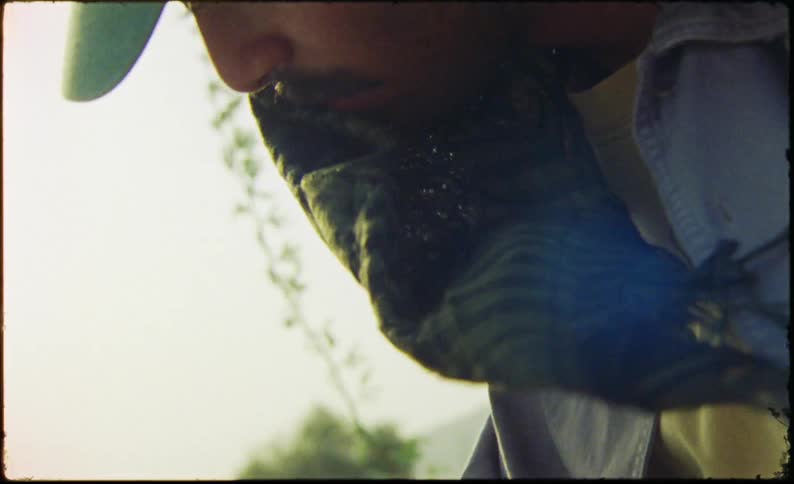 Wind blows the fabric worn under a cap across the face of a man working outdoors