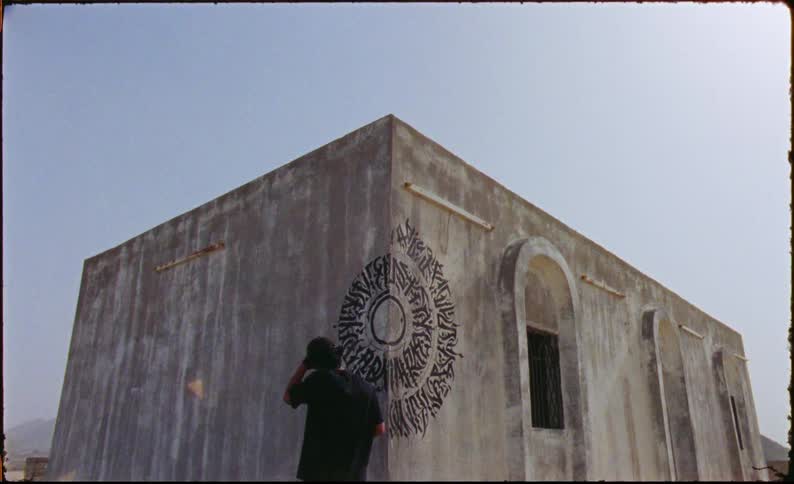 Graffiti artist uses a marker to add to a pattern on the corner of a concrete building