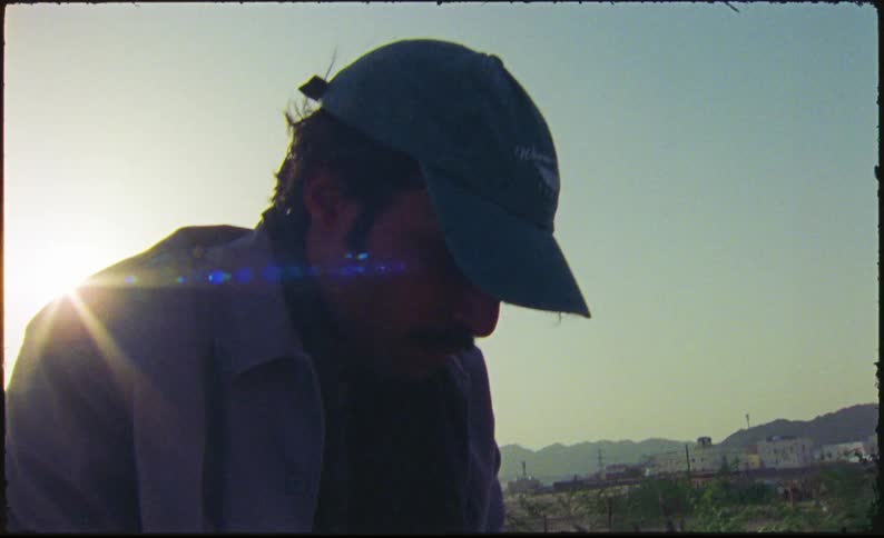 Man in cap sitting on roof of old car reading notebook with notes