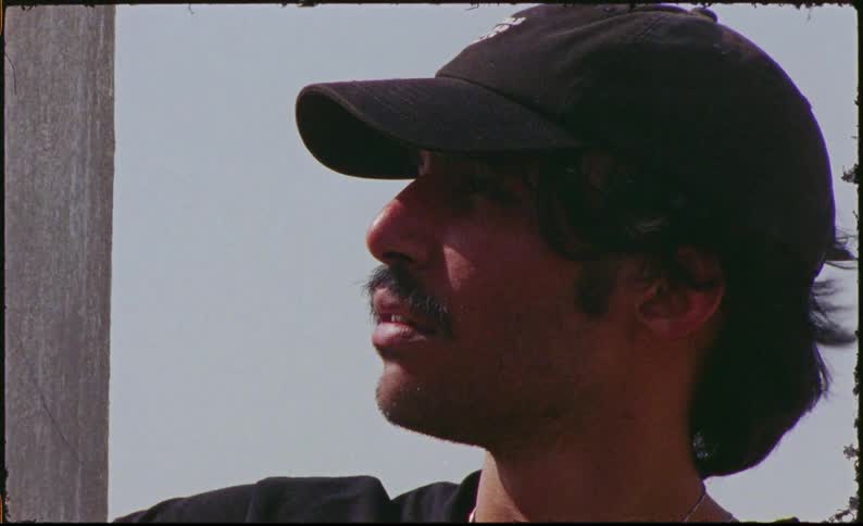 A young man with a black cap and a mustache is looking forward and his hair is blowing in the wind