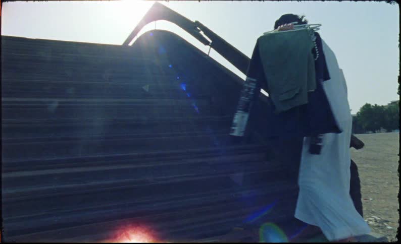 A young man wearing a long white garment is walking up a staircase carrying several pieces of clothing over one shoulder