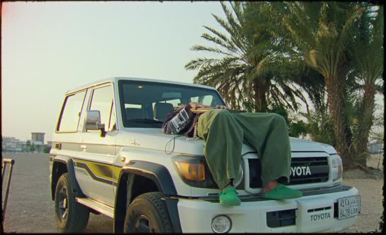 Man laying on hood of toyota car in the desert near palm trees