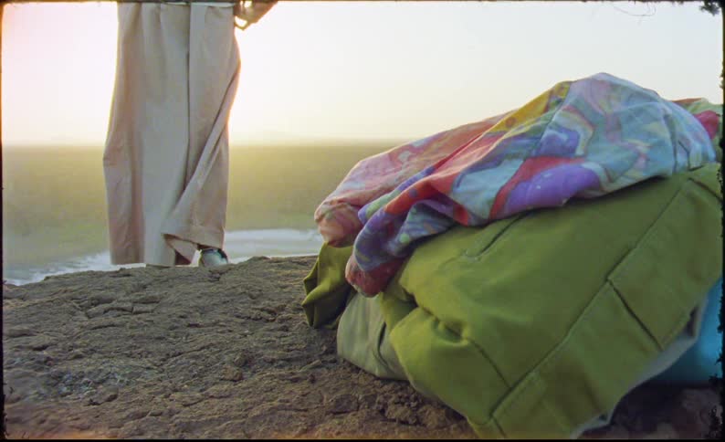Legs of a person wearing a long dress in a natural setting with the sun on the horizon