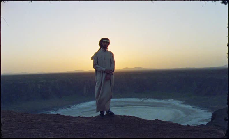 Man in arabic clothing standing on a mountain cliff with sunrise on the horizon