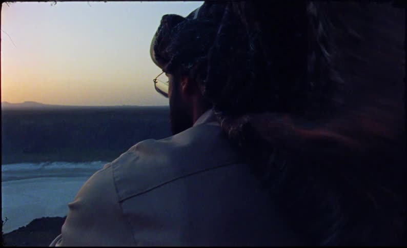 Man sitting on a round mountain enjoying the view of the sunrise on the horizon